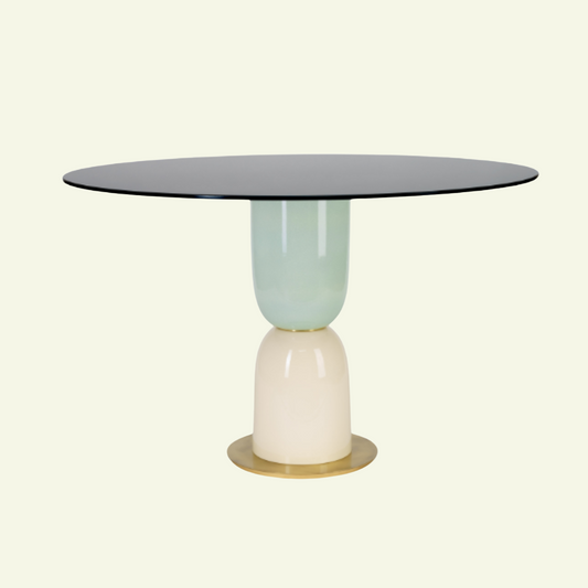 La table ronde Pins de Marioni est juste incroyable ! Son grand plateau en verre rétro-peint noir vient contraster avec son pied en céramique émaillée de forme organique et aux couleurs pastels. Un peu de brillance avec la structure en laiton, et voilà une salle à manger rétro, stylée et surtout exclusive. Cette table faite à la main est signée Marioni, et on leur dit merci !